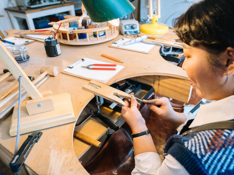 A woman working on a piece of silver jewellery using a variety of specialist tools